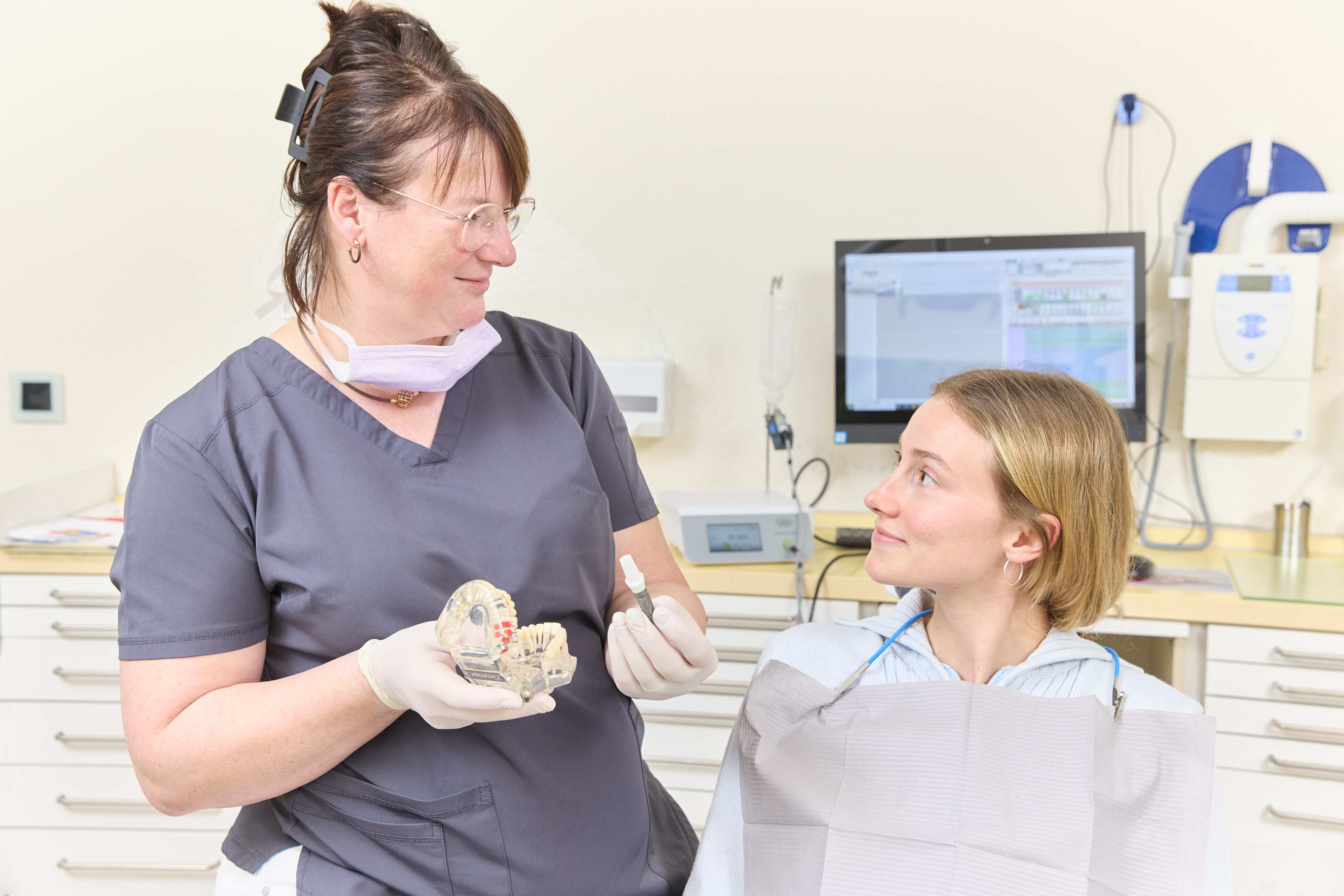 Zahnärztin zeigt einer Patientin ein Modell eines Gebisses